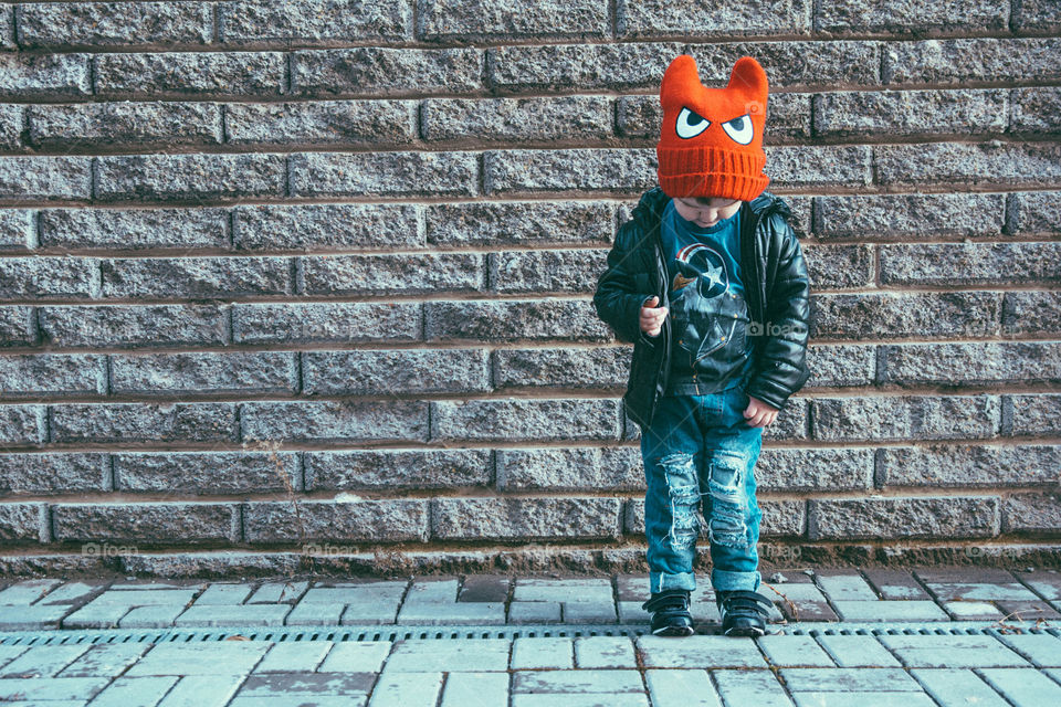 Boy wearing orange woolly hat standing in front of wall