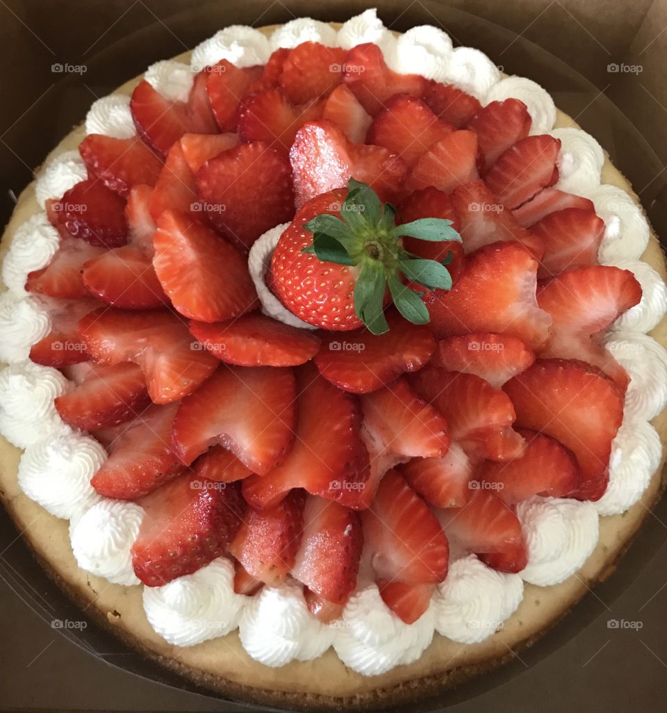 Homemade baked cheesecake topped with homemade whipped cream and fresh sliced strawberries 