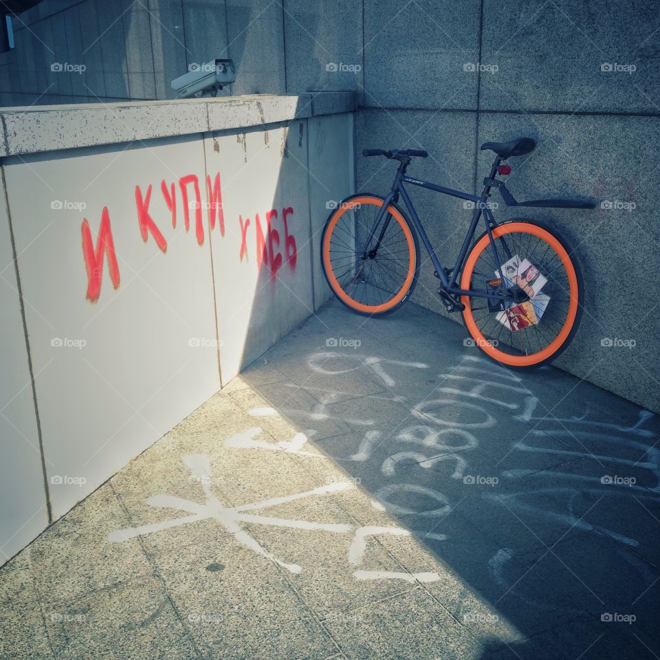 Grey brakeless fixie bike with orange wheels standing near the wall