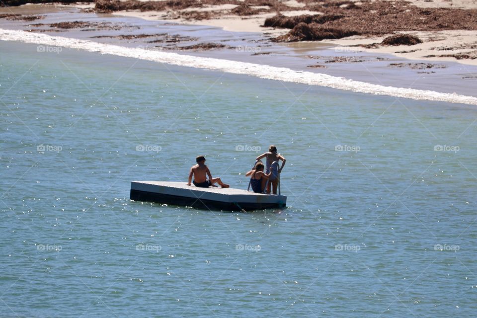 Children having fun on and swimming off of floating raft in ocean