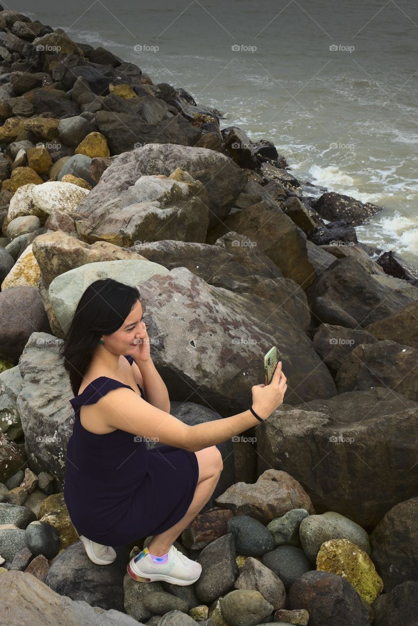 Young woman taking a cell phone picture of herself in front of the sea