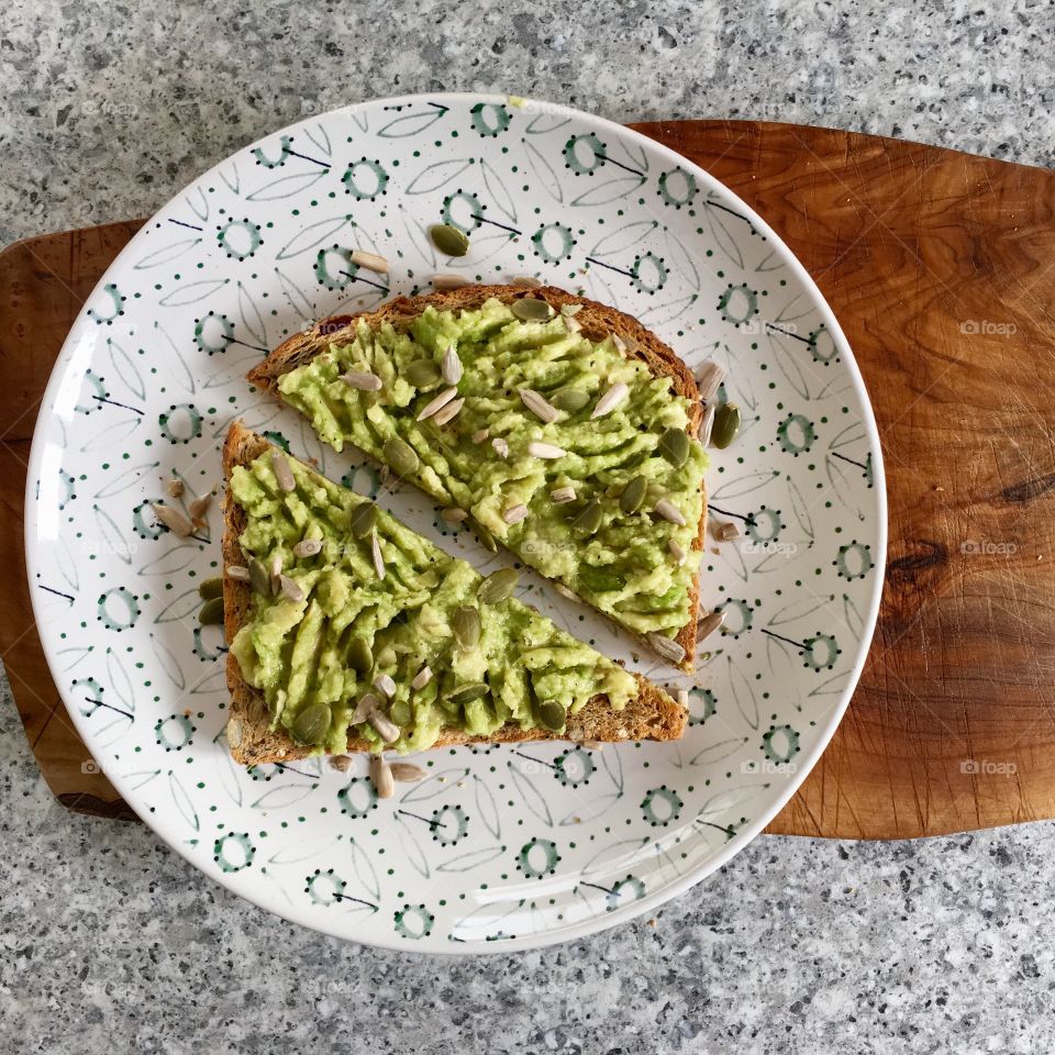 Avocado toast on seeded bread scattered with pumpkin and sunflower seeds and drizzled with olive oil