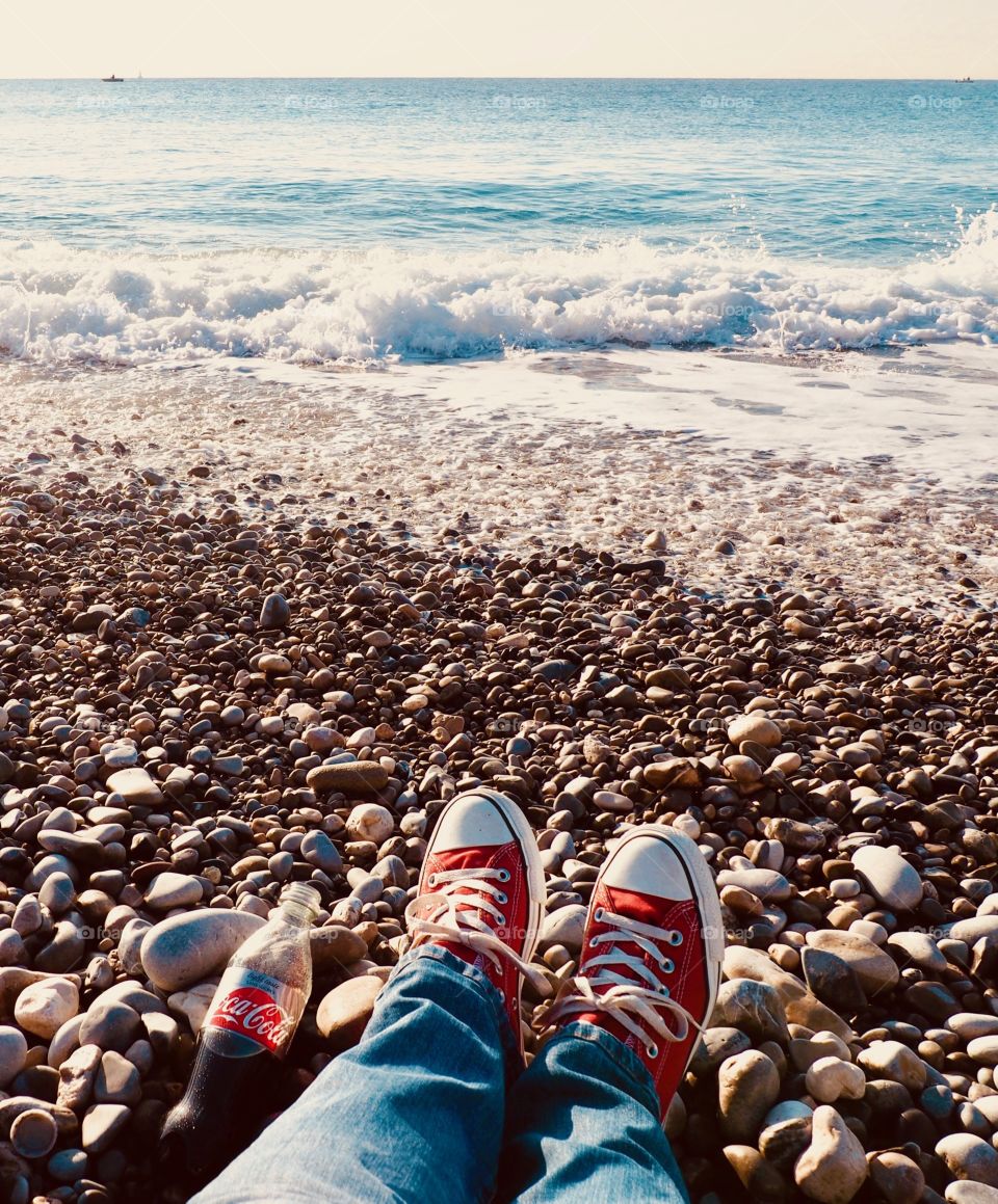 A bottle of Diet Coke  on the beach with red sneakers.