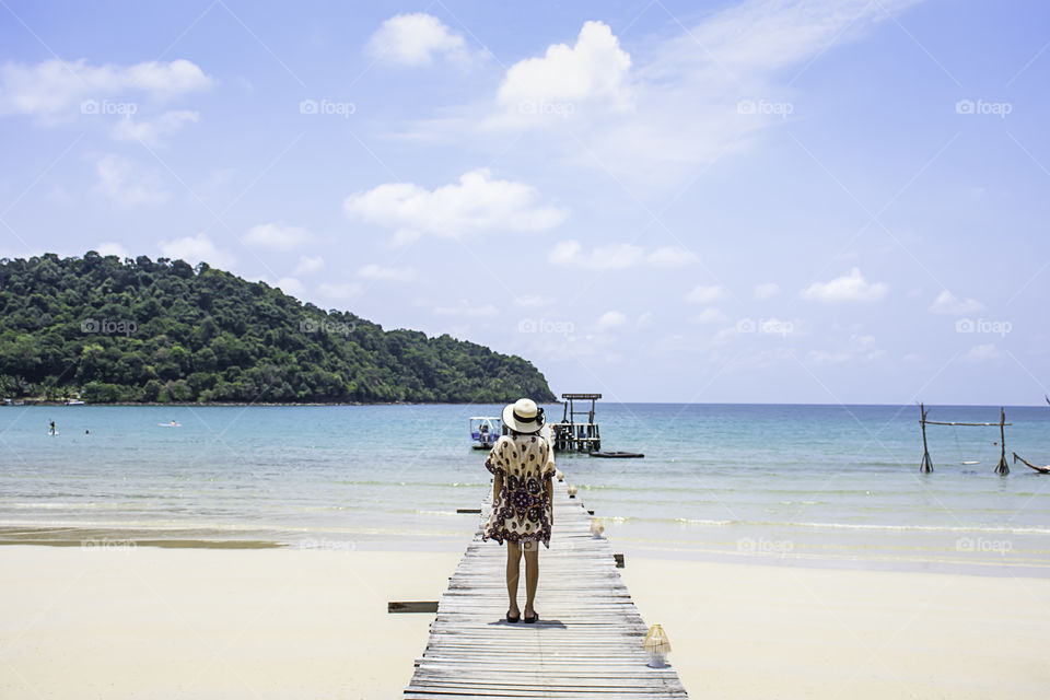 Women Wear a hat on the wooden bridge pier boat in the sea and the bright sky at Koh Kood, Trat in Thailand.