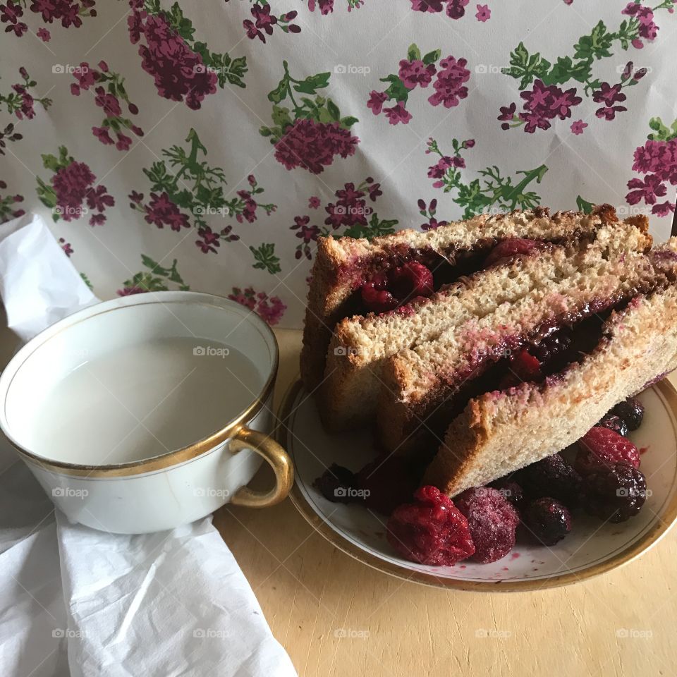 A raspberry and blackberry peanut butter sandwich on a plate next to a teacup on a floral background prepared for lunch. USA, America