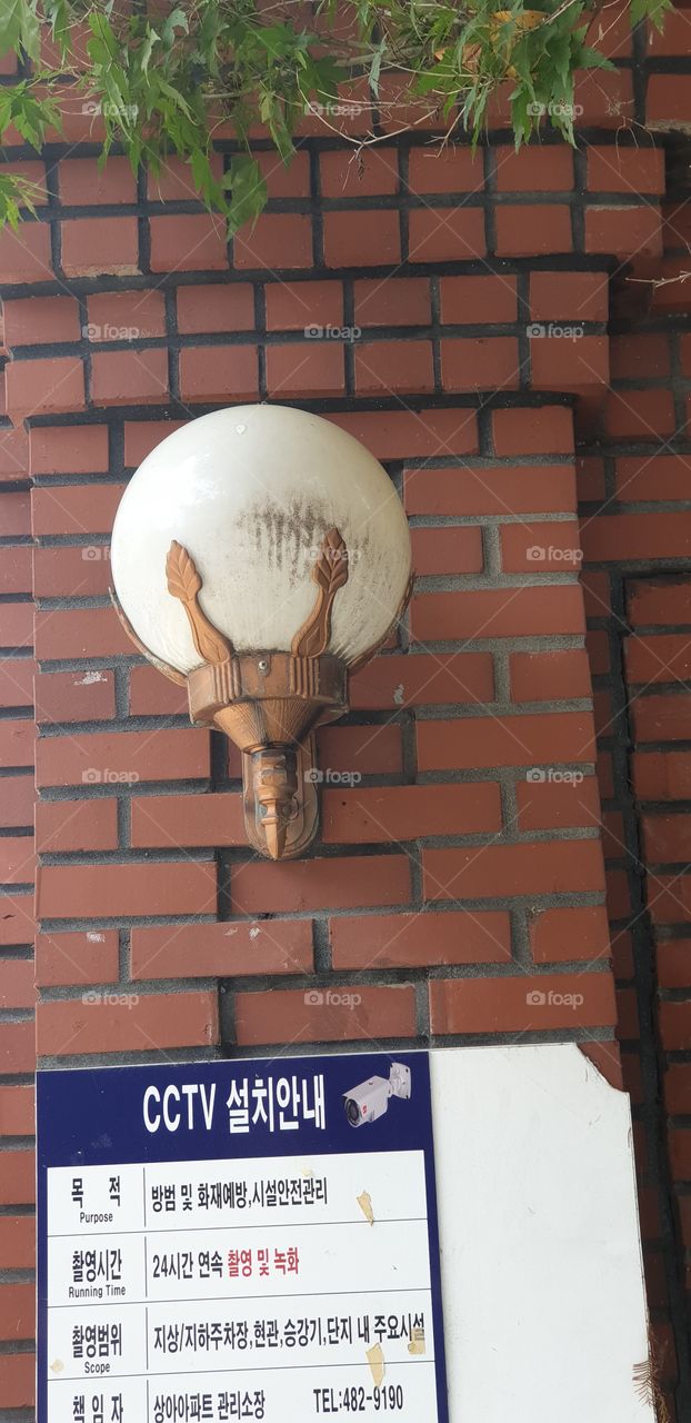 a white glass globe light above a Korean text sign with copper color fitting on a brick wall