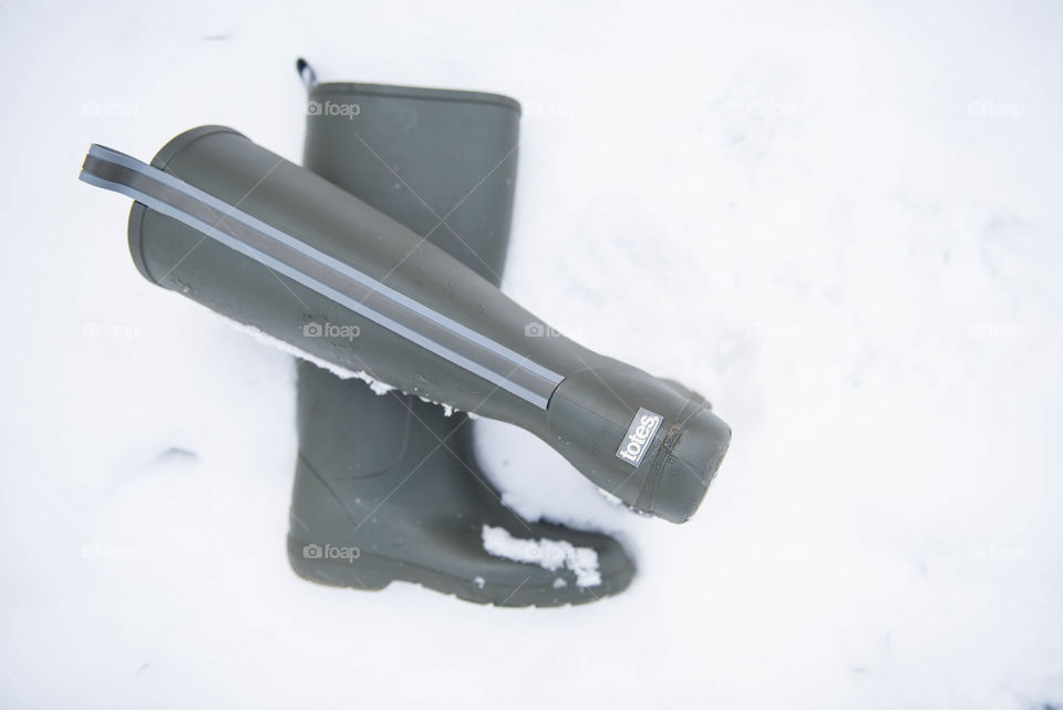 Flat lay of a pair of tall green rainboots in the snow outdoors