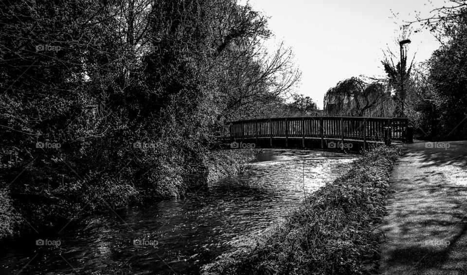 A footbridge crosses a river in England, in black and white.