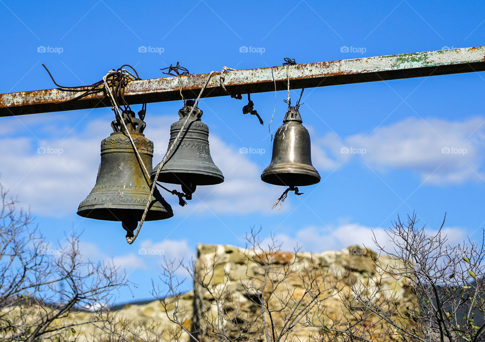 three church bells hanging in chains against a blue sky whit white clouds
