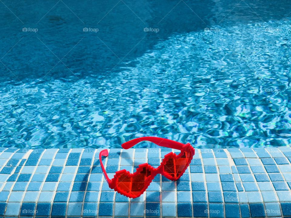 Heart shaped sunglasses on the edge of a pool with turquoise water