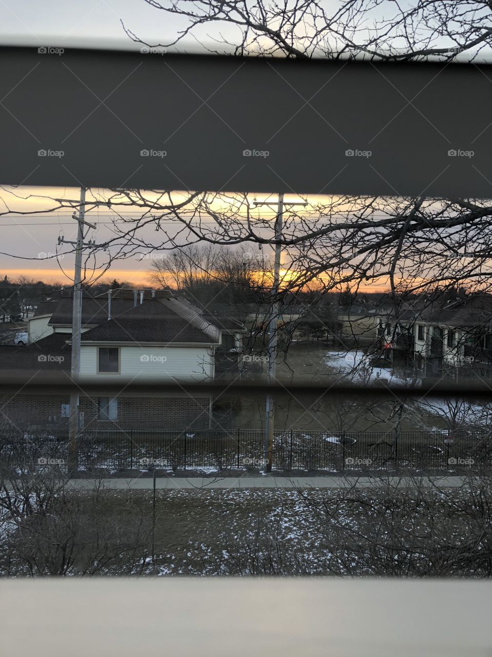 Peeking at sky through bedroom window. Light snow on the ground. Trees, Buildings, & snow 