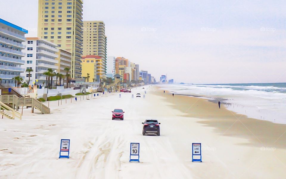 Artistic picture of cars driving down Daytona beach at low tide with speed limit signs in the foreground. 