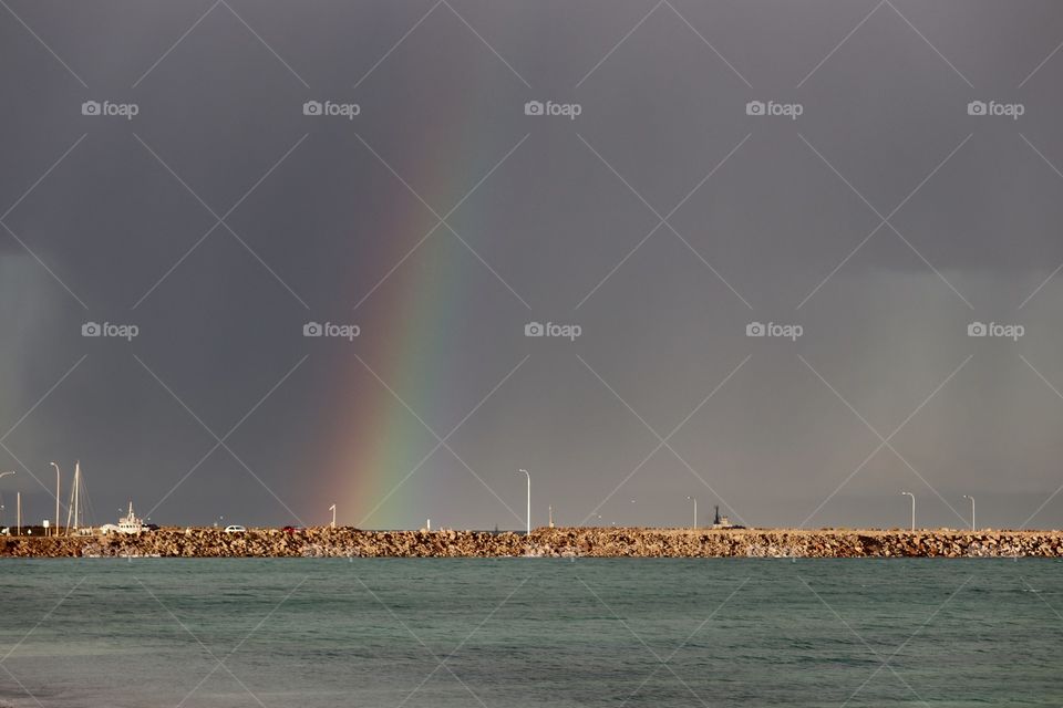 Rainbow in the rain over a harbour and Stone breakwater 