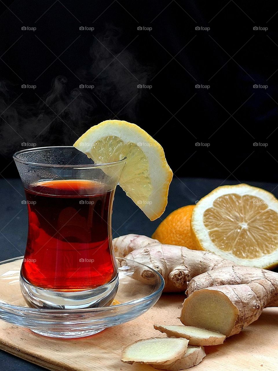 horizontal surface.  Tea in an armuda glass, ginger pieces, ginger root, cut lemon.  Eastern tea.  Steam is visible above the glass of tea.