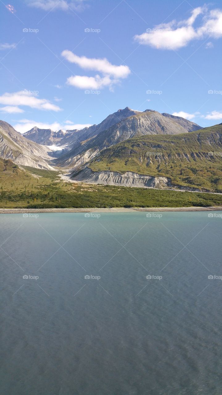 View from cruise ship of ocean and mountains and glacier with blue sky, in Alaska, United States of America, on summer vacation