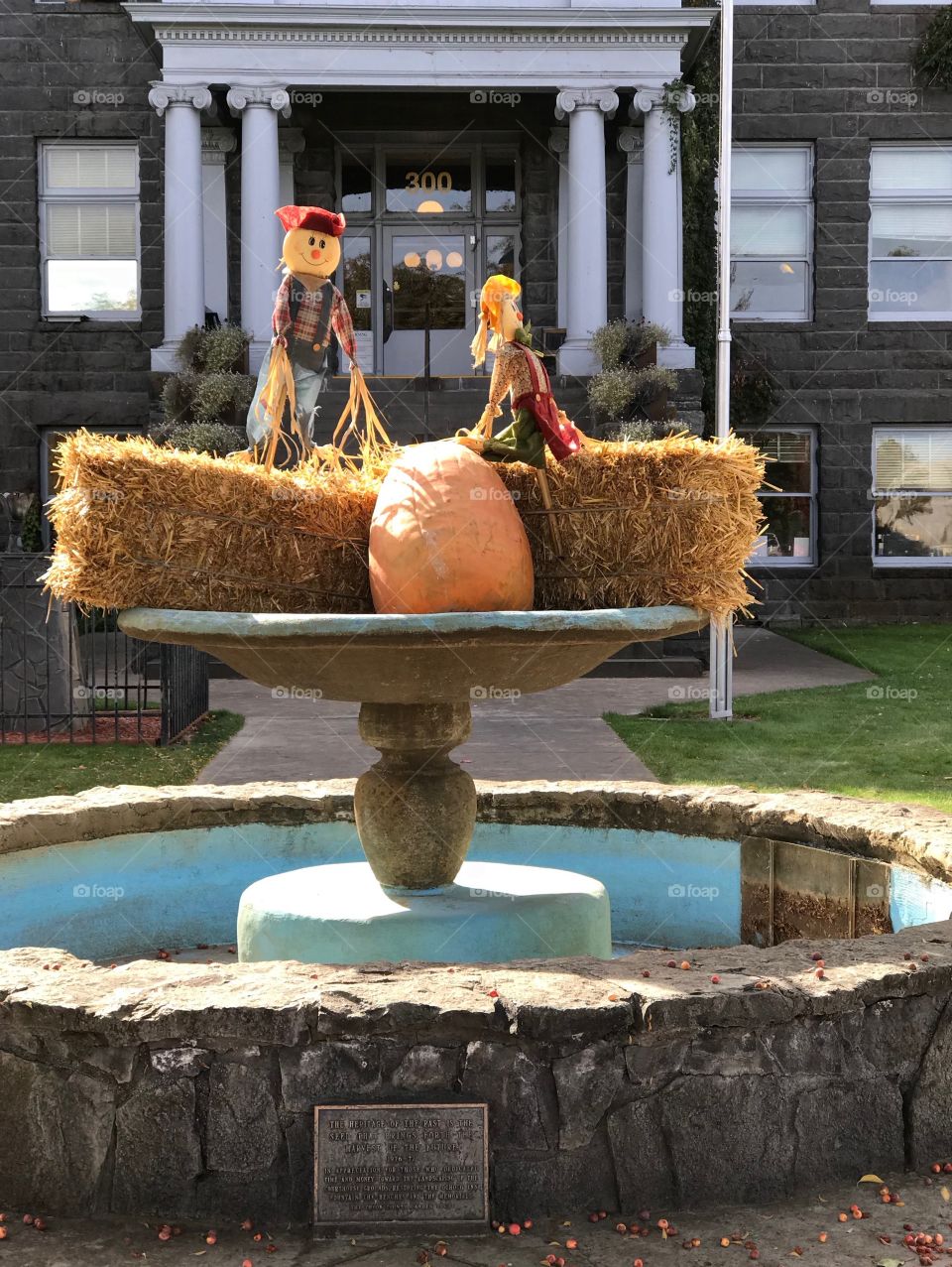 A pair of decorative scarecrows perched on hay bales with a pumpkin in the fountain at the old Crook County Courthouse in Prineville in Central Oregon on a beautiful fall day.