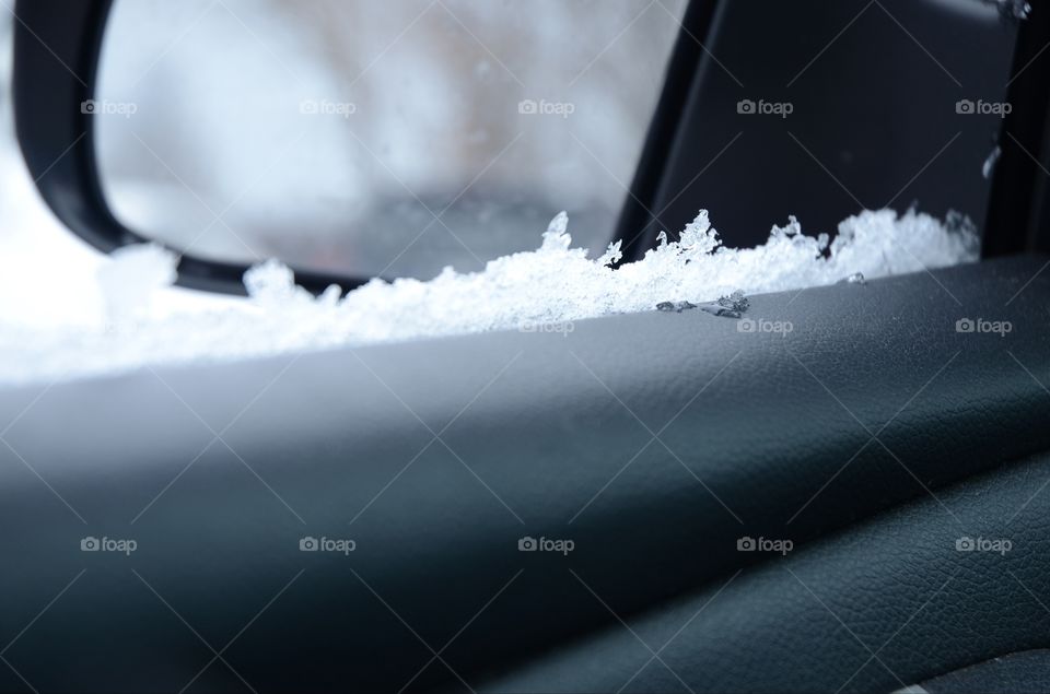 Snow and ice sit on a car door window seal during the wintry season.
