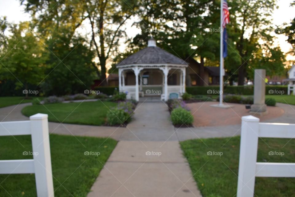 Sidewalk leading up to a gazebo in the summer evening, surrounded by flowers and trees. 