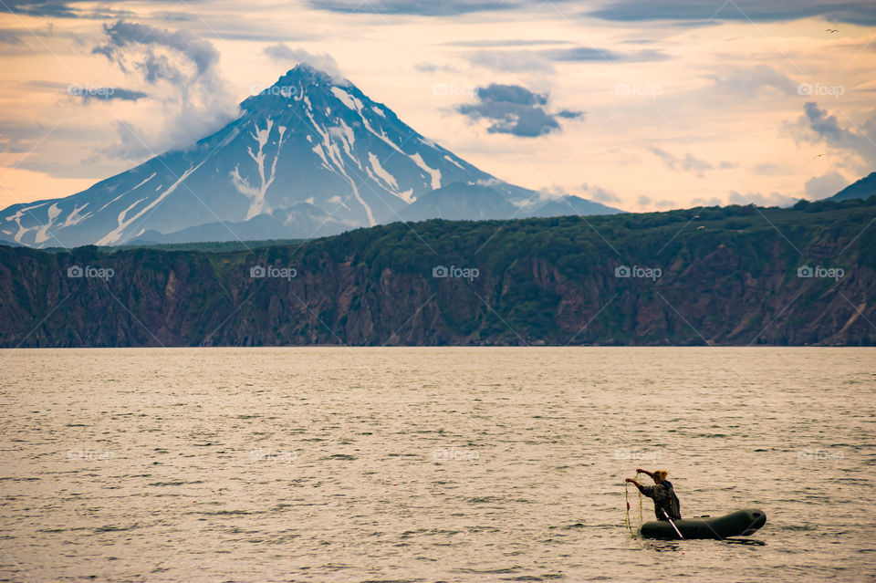 A woman in a boat fishing in the bay of the Pacific Ocean on the background of mountains and Vilyuchinsky volcano