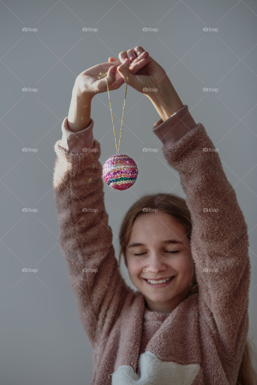Portrait of young happy smiling girl wearing warm sweater and enjoying her handmade colorful Christmas decoration ball