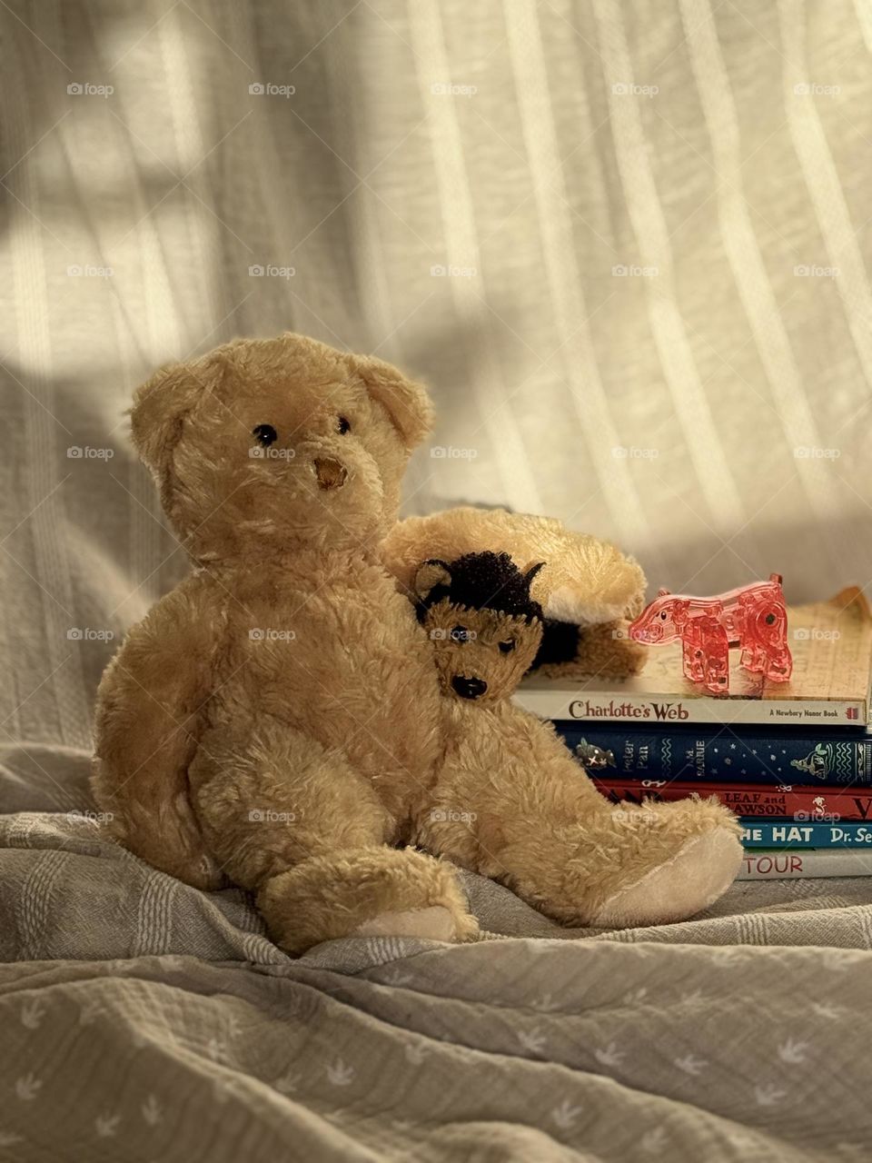 Well-loved teddy bear and wolf stuffed animals with a pink plastic pig posed on a stack of children’s books with neutral fabric background