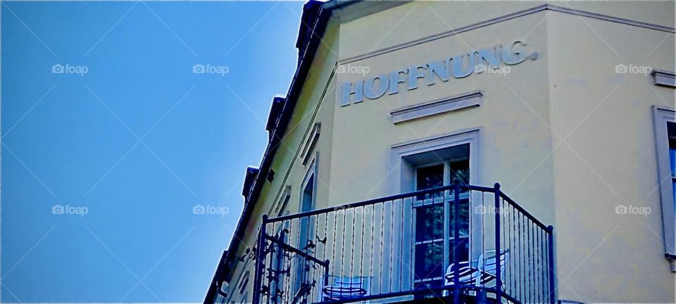 The upper floor of the guesthouse shown previously with a balcony. A cast iron railing protects the hotel guests from falling. 2022. Hypnotic Productions