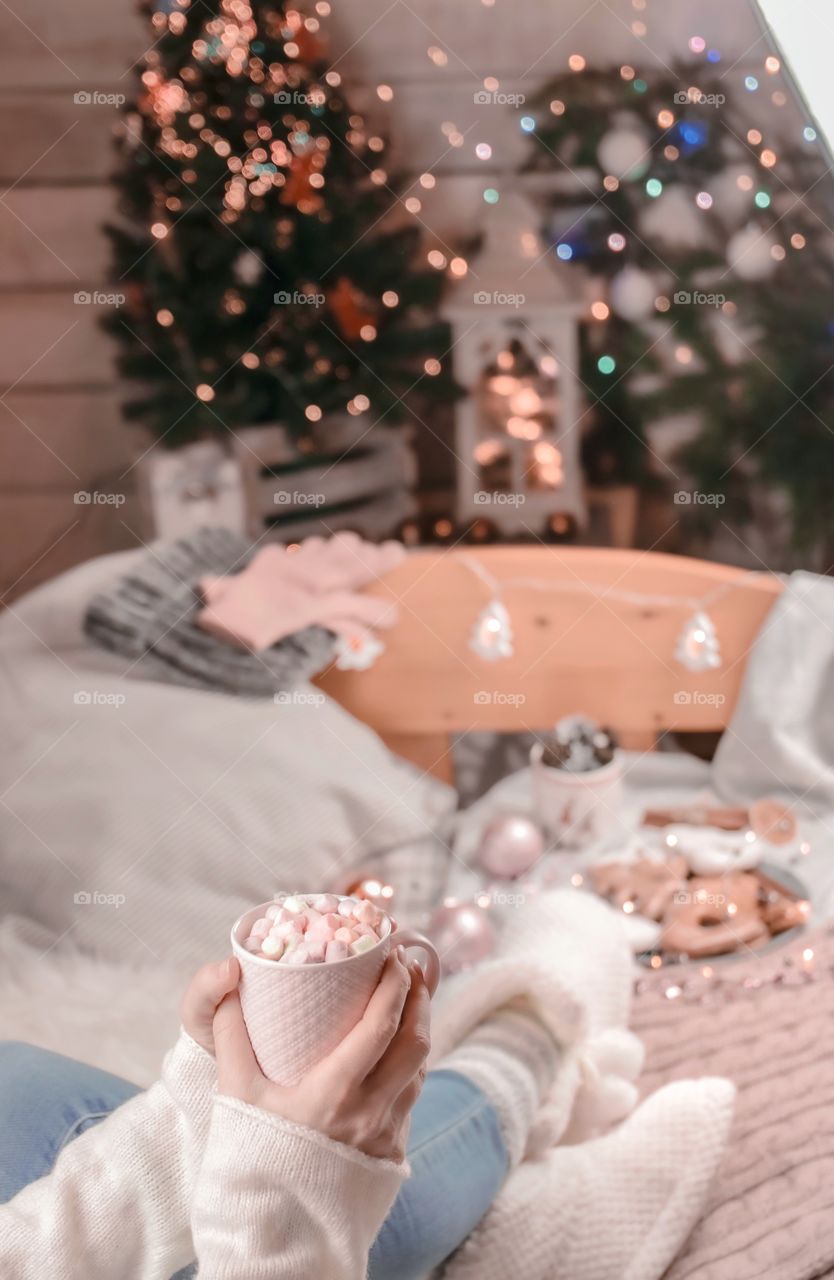 Cup with marshmallows in female hands on a background of Christmas decor