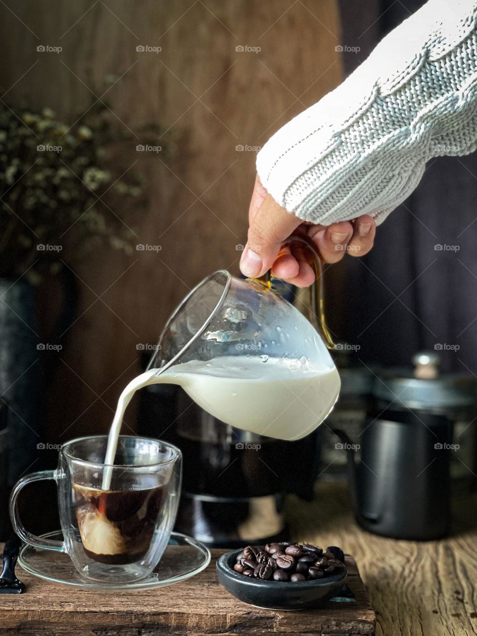 Pouring milk into a clear cup of black coffee in close up view