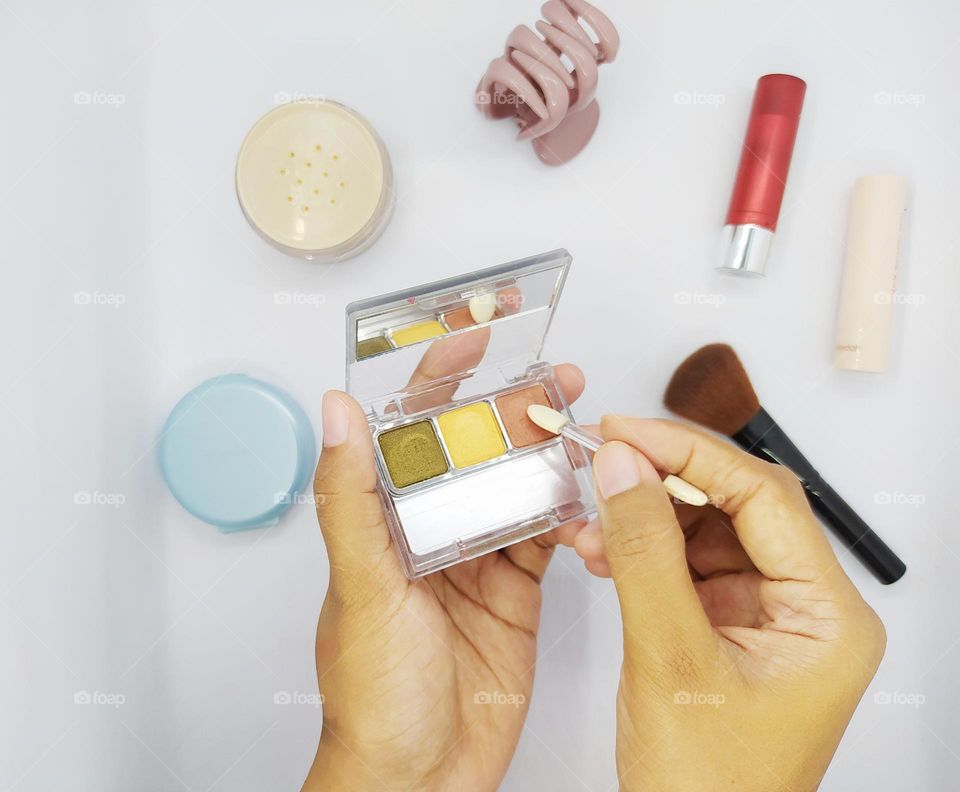 The hand holding the eyeshadow kit applicator.  makeup tools on a white background