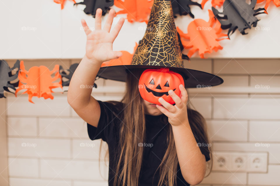 Little girl dressed as a witch for halloween holding a pumpkin with a face on the background decor