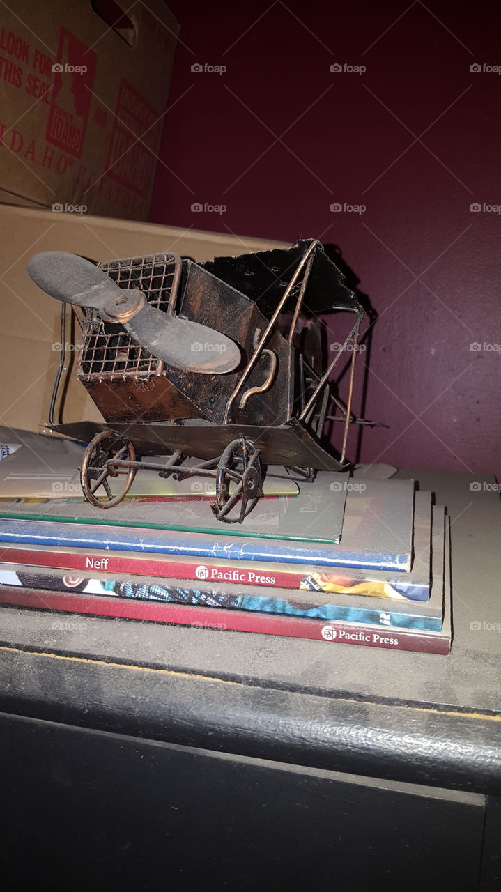 This old rustic brass airplane toy is sitting upon some thin books on top of a closet. Old and vintage.