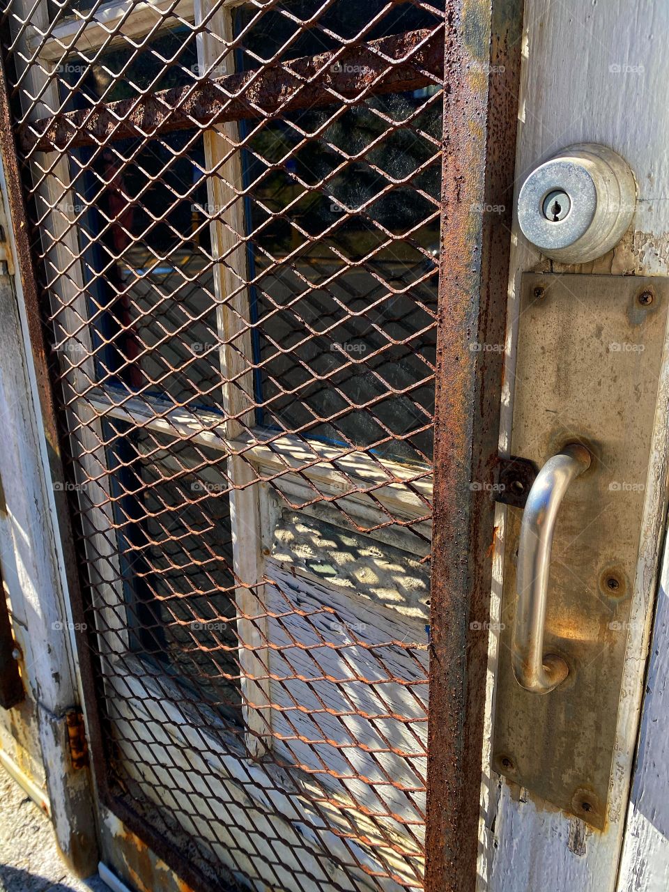 An old entrance to an abandoned train station is locked up and the window covered with a grate that has rusted. 