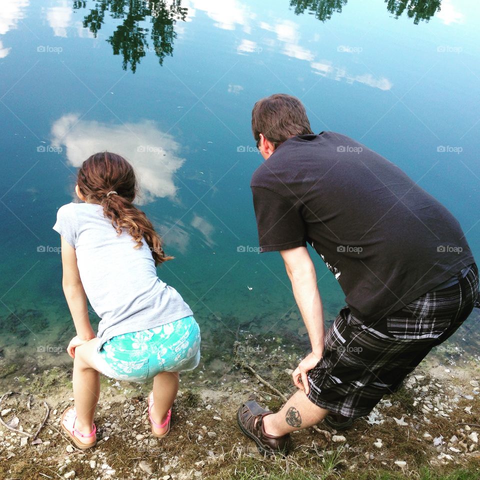 Dad and daughter at the pond w the sky reflecting. 