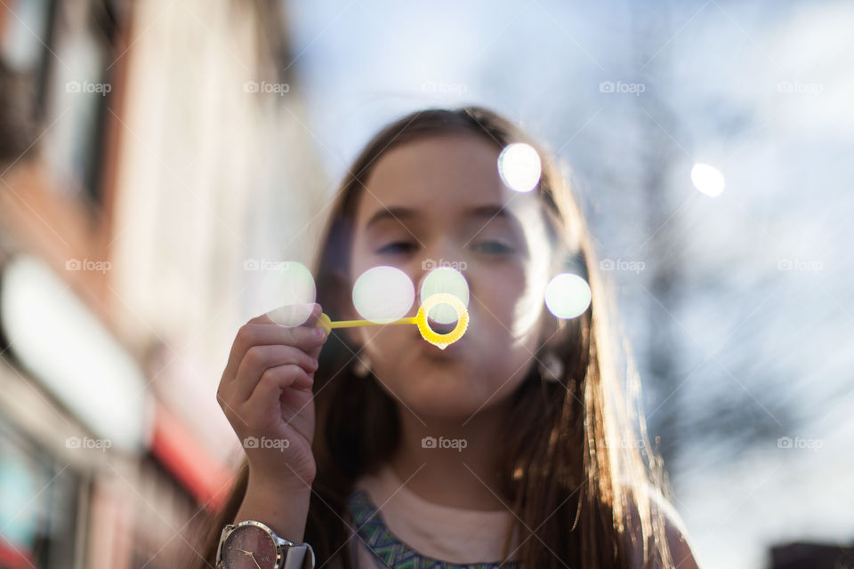 Pretty brunette girl blowing bubbles that sparkle like glitter outside on the street in the city. 