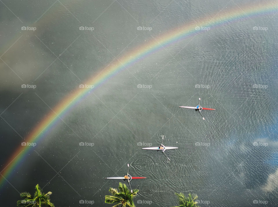 A rainbow and clouds reflected on water where three scullers are rowing