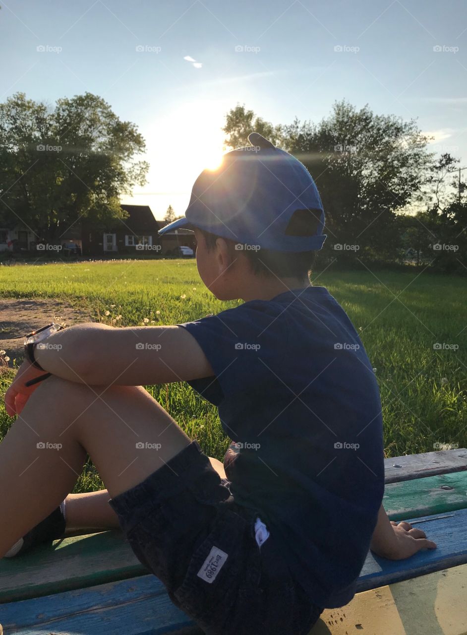 Boy sitting on a park bench at sunset