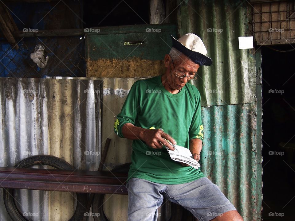 an old asian man playing crossword puzzle on a newspaper