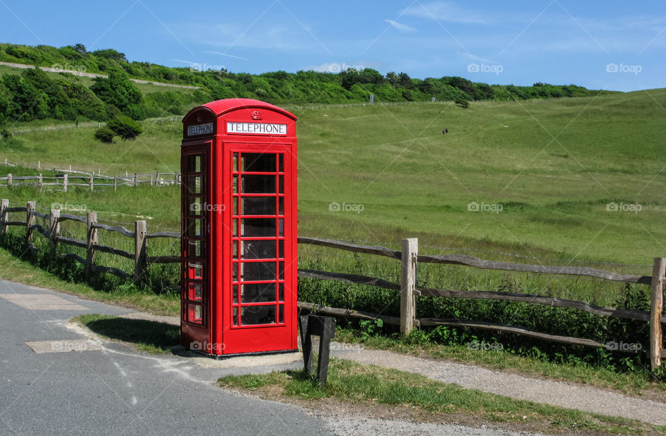 A red, old style, UK telephone box stands in contrast to the green field it is placed next to