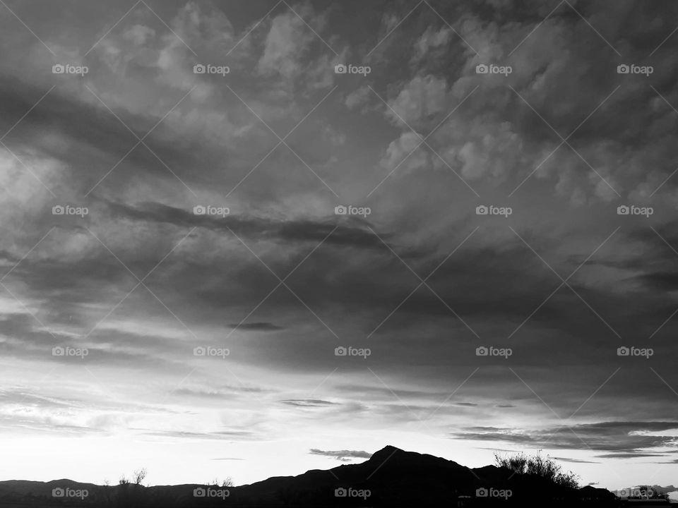 A black and white photo of a cloudy sky with a mountain below. 