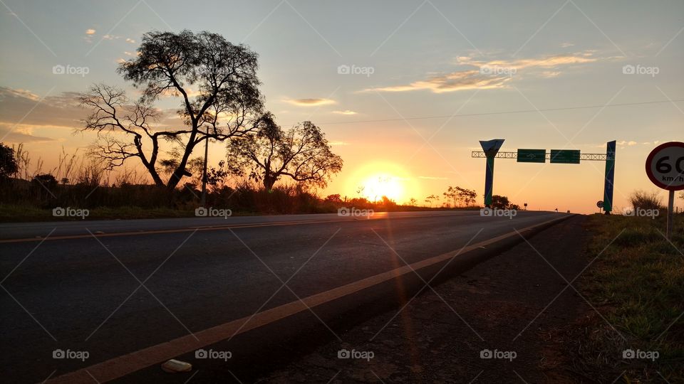 Um por do sol, nuvens, árvores e rodovia.