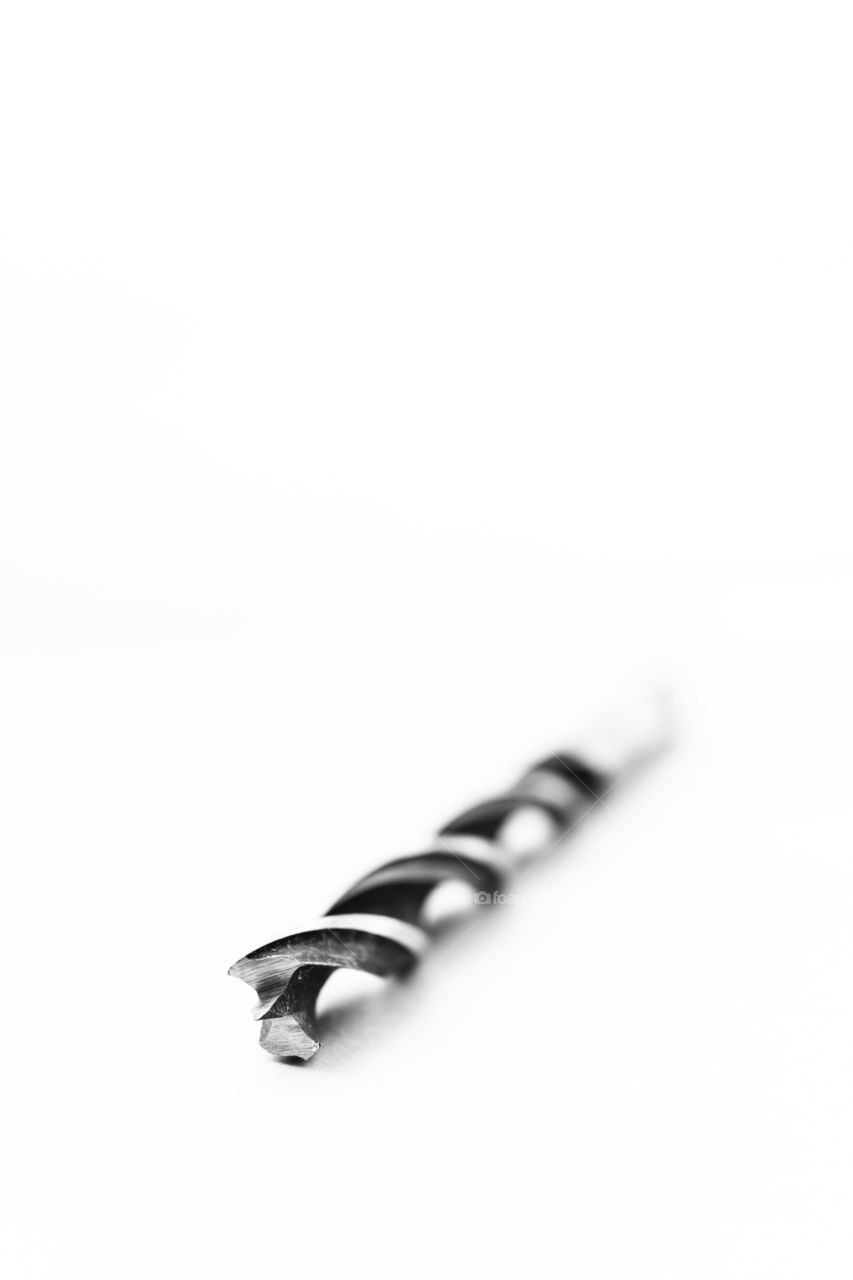 A close up black and white portrait of a metal wood drill bit. the dril is shaped as a swirl to remove wood chips from the drilling hole.