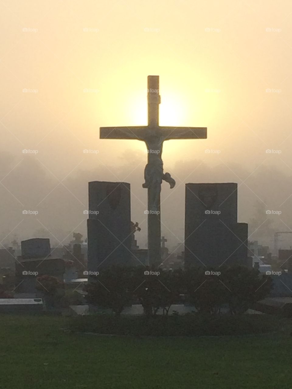 Foggy sunrise over cemetery sun lighting the cross