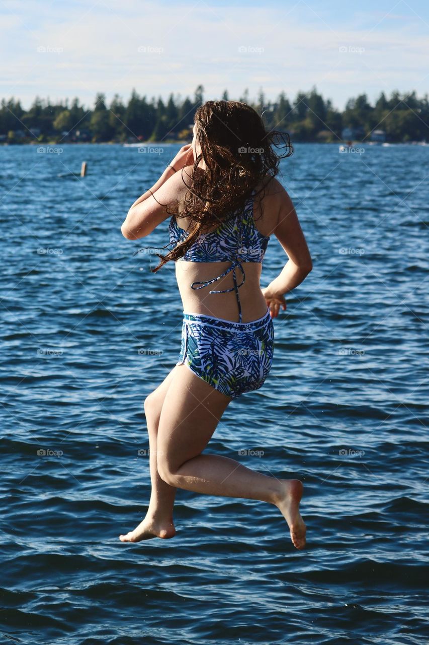 A young girl enjoys Summer weather as she jumps into the clear, blue water of American Lake in Washington State