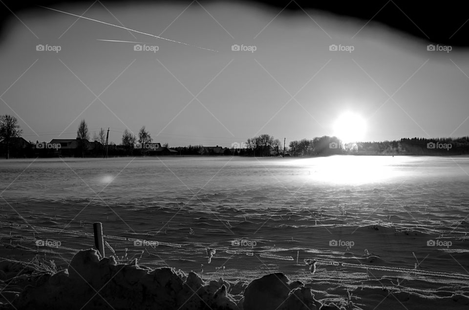 A  nostalgic snowy field by a sleepy countryside village at sunset in black and white. 