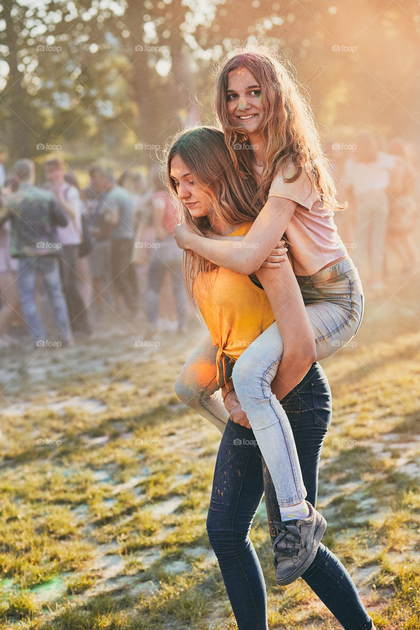 Portrait of happy smiling young girls with colorful paints on faces and clothes. Two friends spending time on holi color festival. Real people, authentic situations