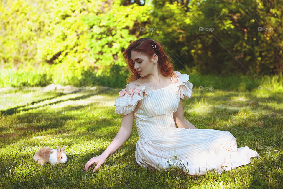 Funny redhead woman playing with rabbit in the sunny day in spring. Lifetime. Outdoor activities