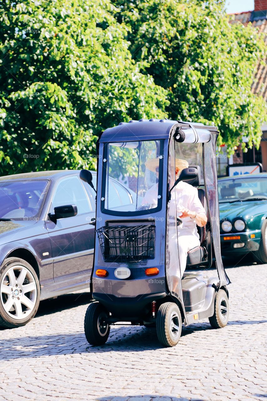 Person driving around on the street a sunny summerday in a very small vehicle on four wheels 