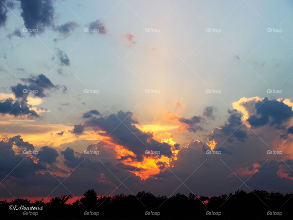 Stopped on a turnpike to catch the sun going down amid the clouds, noticing the sun looked like a heart with golden rays shooting up from the heart!!