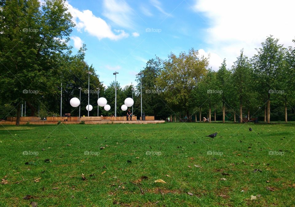 Modern art and stage in park in summer, green, blue sky with clouds, trees and birds