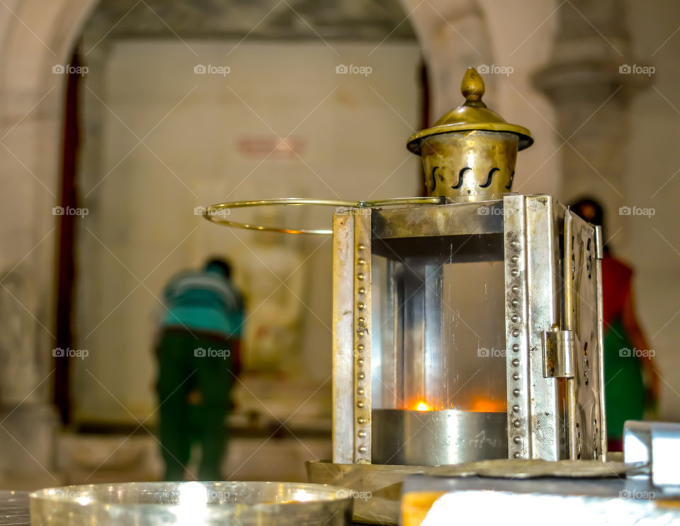 Beautiful Design of Luxury Metallic Lighting Lamp inside Jain temple. White marble sculpture of Jain tirthankara in meditation in a blurry background.